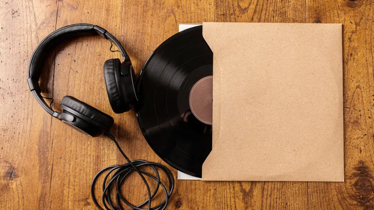 Illustration : casque audio noir et disque vinyle sortant d'une pochette kraft sur une table en bois, pour un nouveau titre